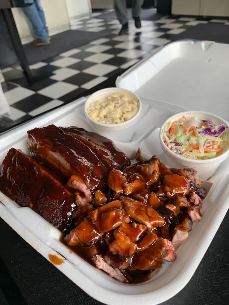 A CJ's takeout tray of ribs and chopped beef with mac salad and slaw on the checkerboard floor